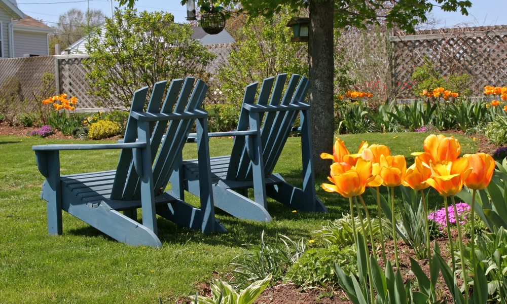 Two Adirondack chairs accent artificial grass in a springtime backyard