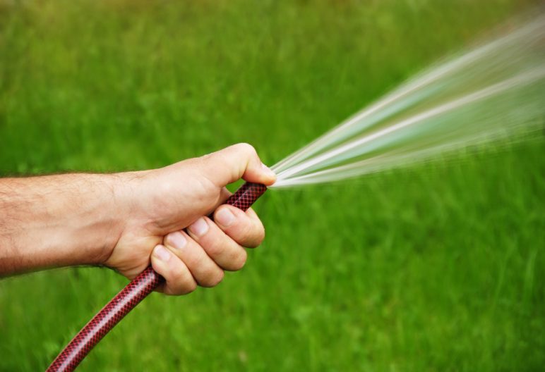 Woman waters artificial grass lawn with a hose